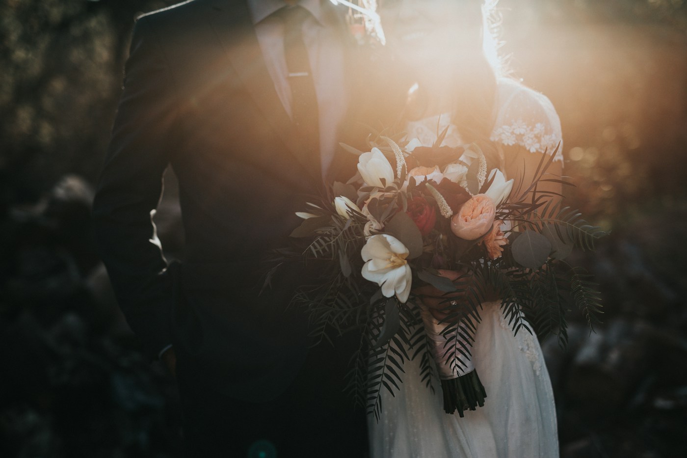 A sunlit wedding couple holding an elegant bouquet of white and blush flowers